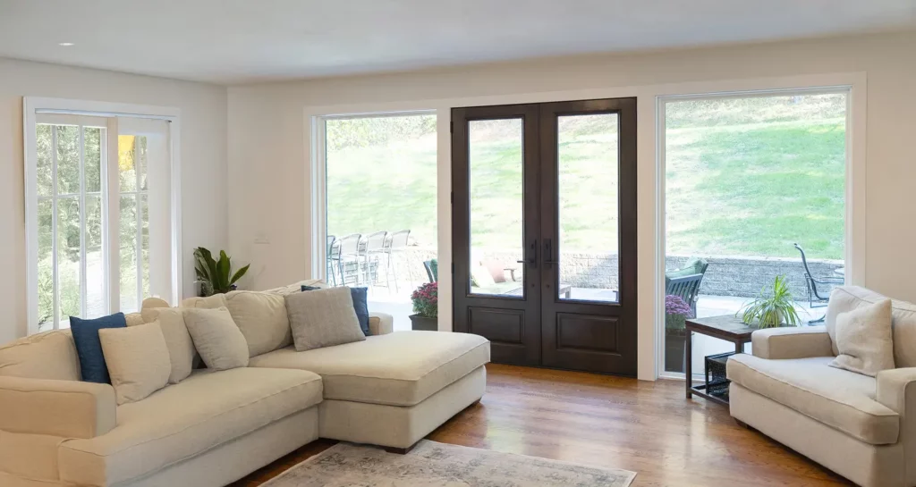 Bright living room with beige sofas, large windows, and double wooden doors to a patio.