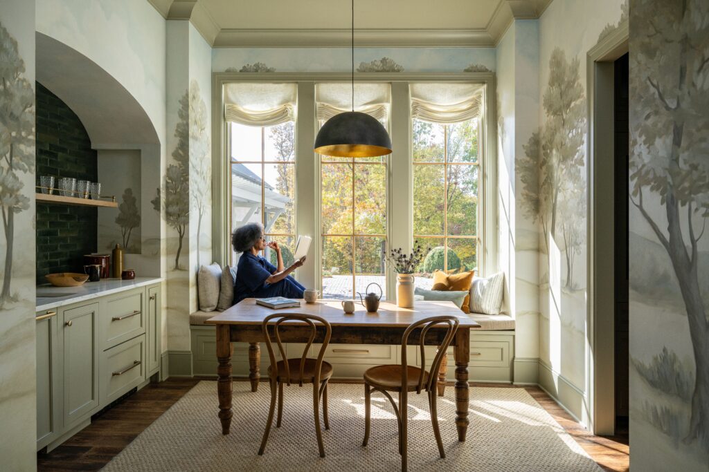 A dining nook with tall windows, where a woman sits reading.
